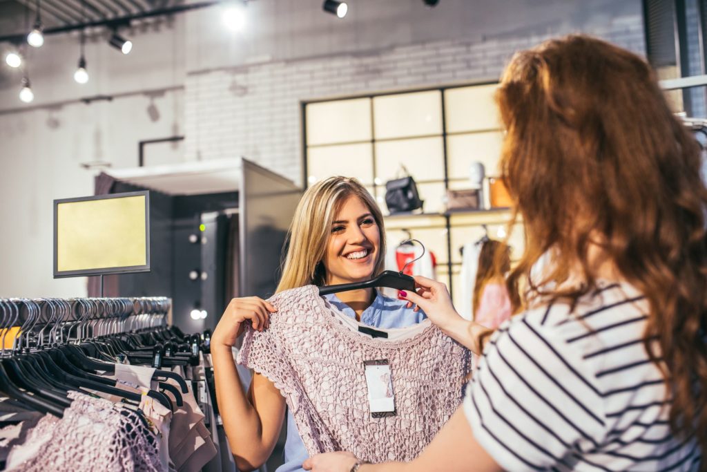 Vendedora de loja ofertando roupas para sua cliente e evitando comportamentos inadequados diante de um cliente