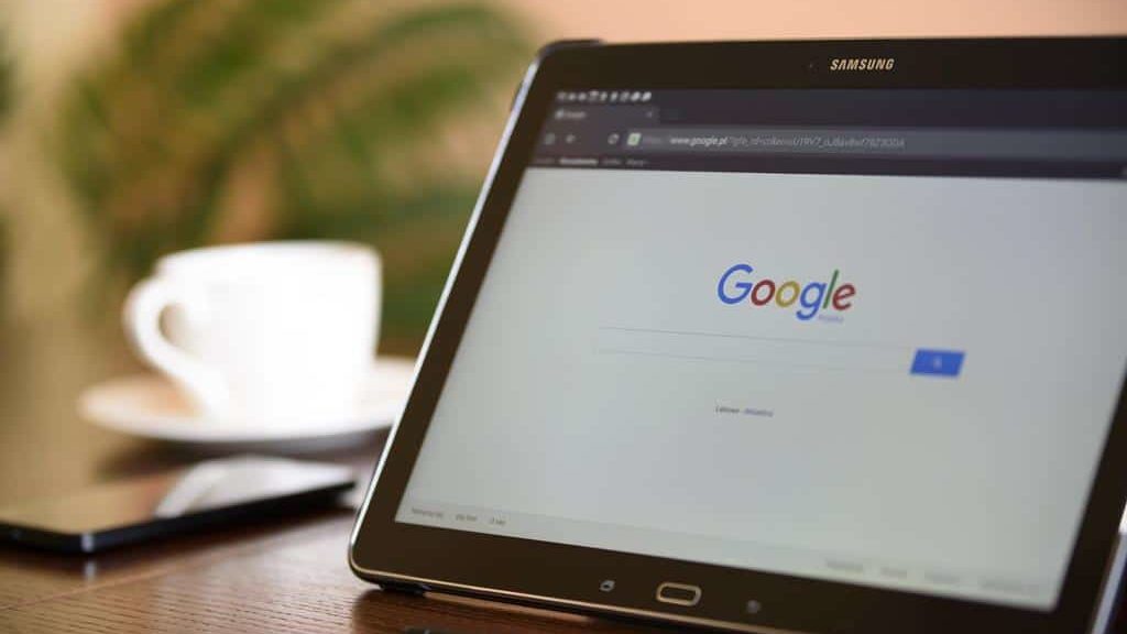 Tablet exibindo a página inicial do Google sobre uma mesa, representando buscas online e a importância do SEO para melhorar o posicionamento de sites nos resultados de pesquisa.