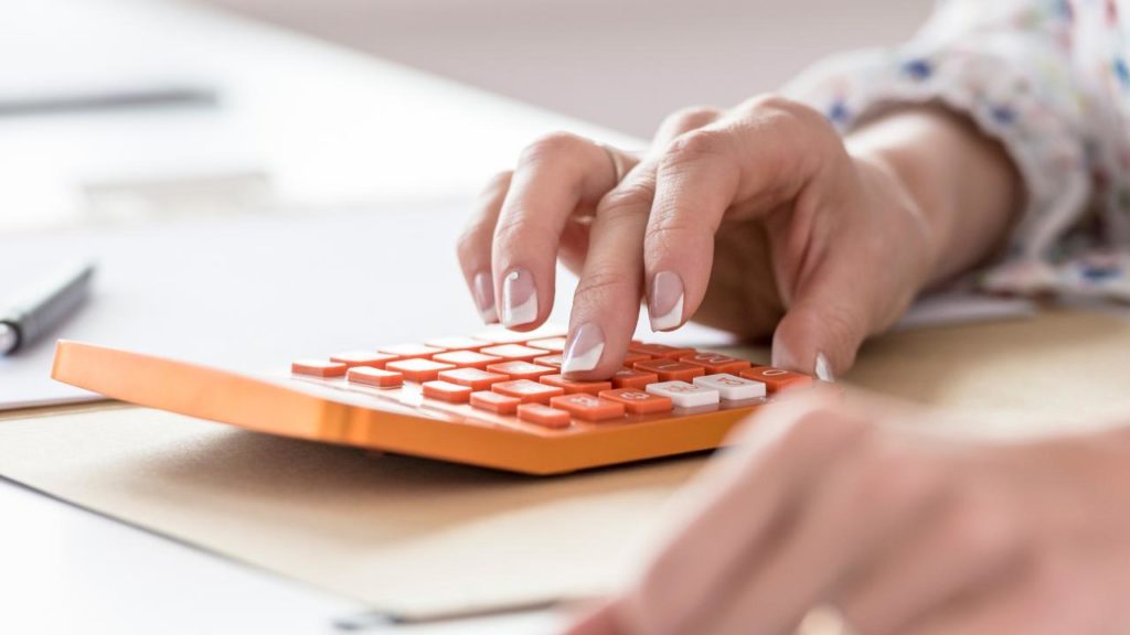 uma pessoa realizando cálculo em uma calculadora colorida, sobre a mesa
