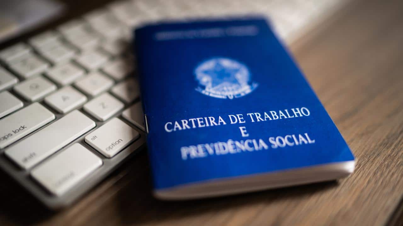 carteira de trabalho sobre um teclado de computador, ambos estão em cima de uma mesa