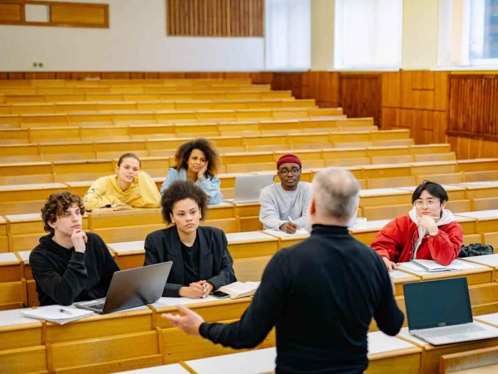 Alunos reunidos assistindo um evento acadêmico ministrado por seu professor.
