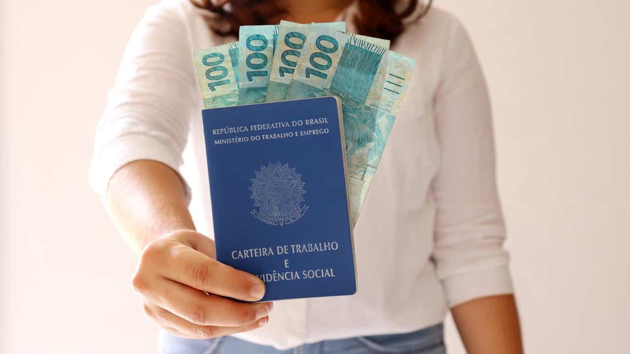 uma mulher com uma carteira de trabalho e várias cédulas de dinheiro na mão