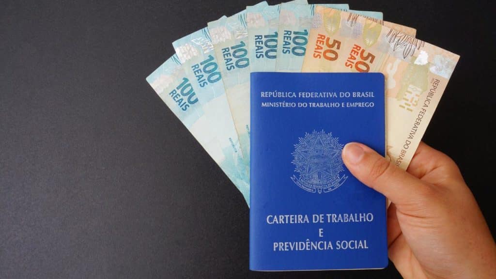 carteira de trabalho e várias cédulas de dinheiro nas mãos de uma pessoa, simbolizando o seguro-desemprego