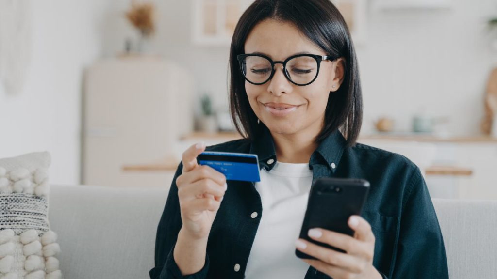 mulher com cartão do banco em uma dar mãos e o celular na outra.