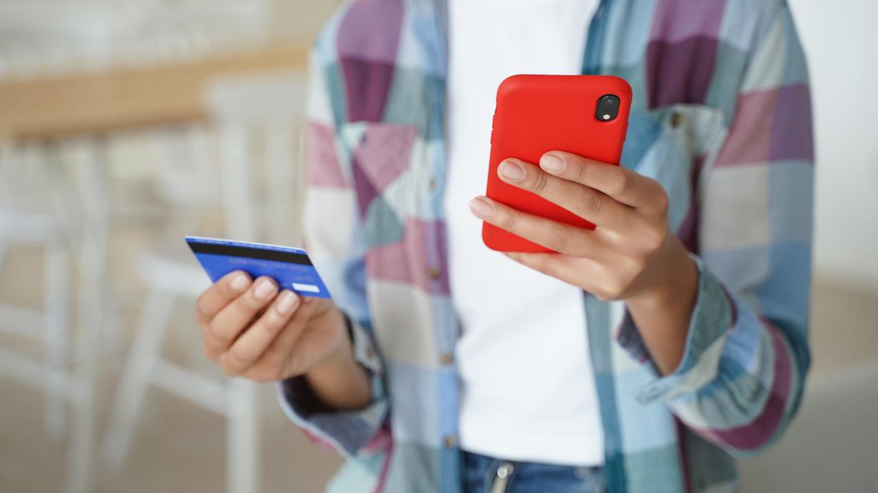 pessoa com o celular e cartão do banco nas mãos, realizando solicitação de seguro-desemprego