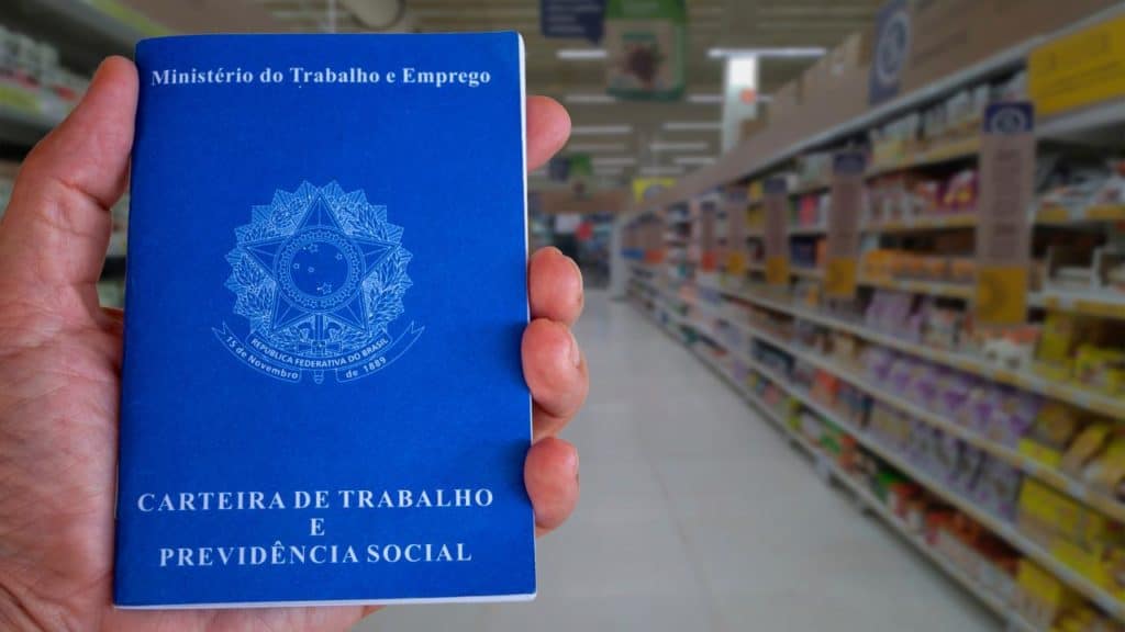 carteira de trabalho na mão de uma pessoa, e uma loja ao fundo da imagem