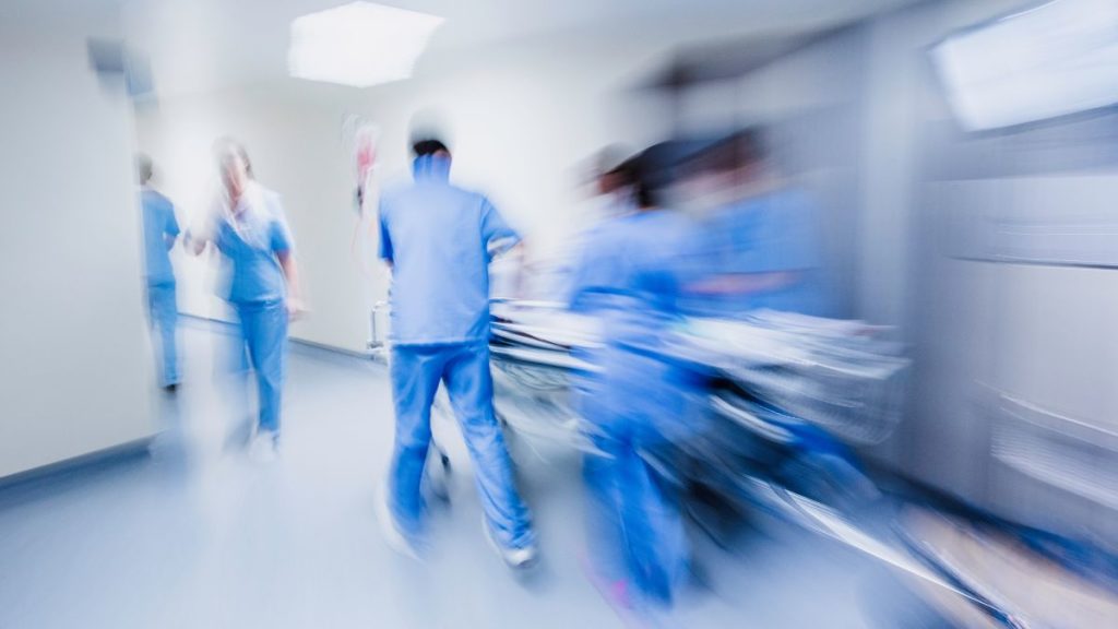 médicos e socorristas empurrando uma maca em um corredor de hospital. 