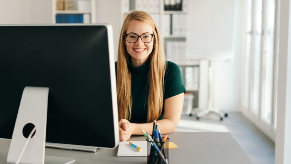 recepcionista sentada em seu computador sorrindo.