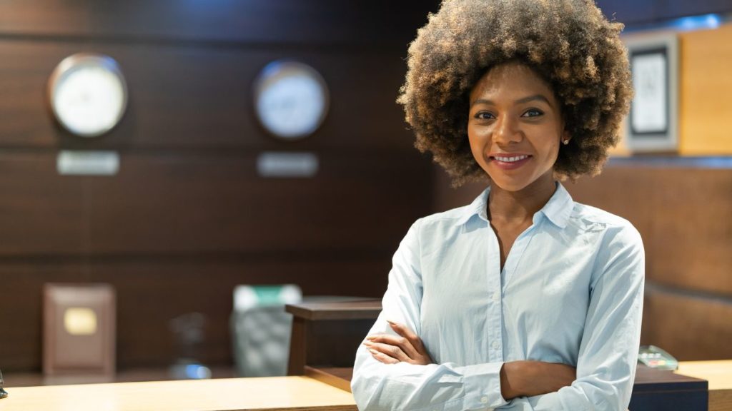 recepcionista de braços cruzados sorrindo em seu local de trabalho.