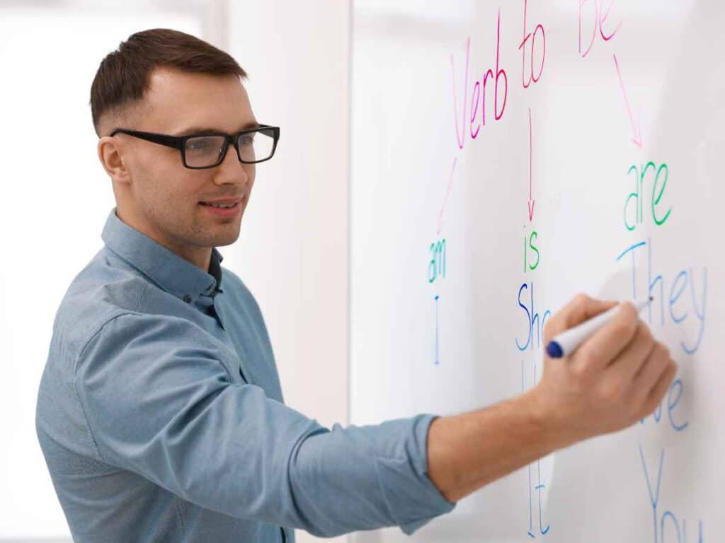 Professor escrevendo em um quadro branco a conjugação de um verbo