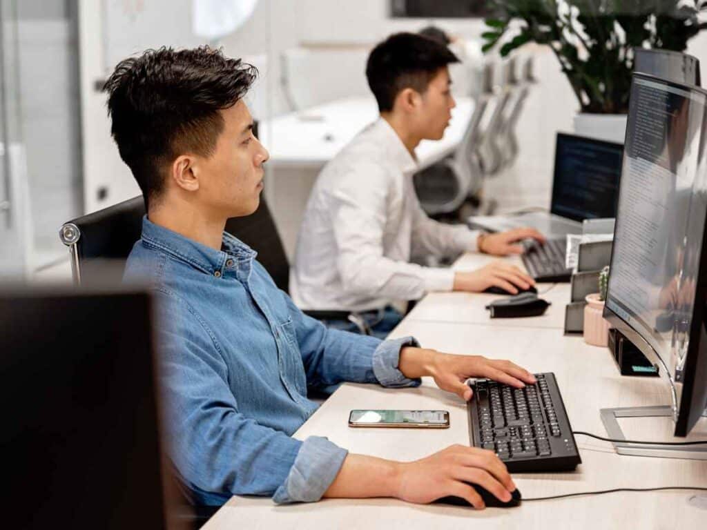 Funcionário do governo monitorando através de ferramentas específicas os vínculos que um beneficiário do seguro-desemprego tem. Ele usa uma camisa azul e faz esse monitoramento através do computador.