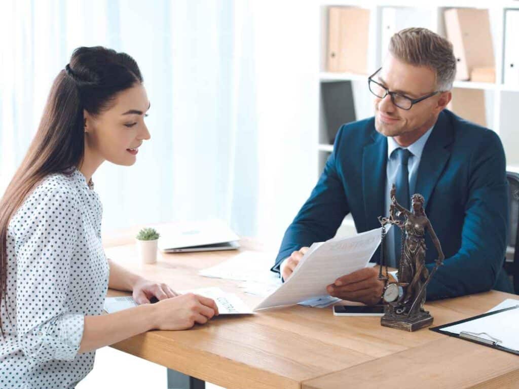 Advogado em seu escritório conversando com uma cliente, explicando de forma clara o que é o seguro-desemprego. Ele apresenta um papel com informações ilustrativas sobre o benefício, enquanto a cliente o escuta com atenção, buscando entender seus direitos.