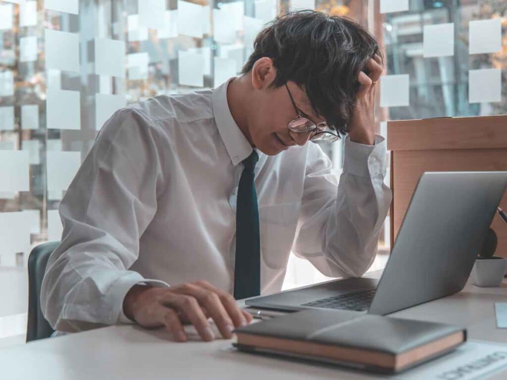 Dono de empresa olhando fixamente para a tela de seu notebook após receber uma notificação de que poderá ser penalizado judicialmente por ter realizado um acordo ilegal com um ex-funcionário. A expressão séria revela preocupação diante das possíveis consequências legais.