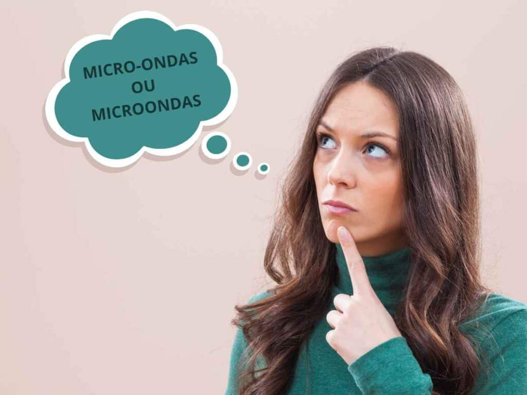 Mulher com uma expressão reflexiva, pensando na forma correta de escrever microondas ou micro-ondas. Ela usa uma blusa ver e tem um balão de pensamento escrito "Micro-ondas ou Microondas". Fundo bege sólido