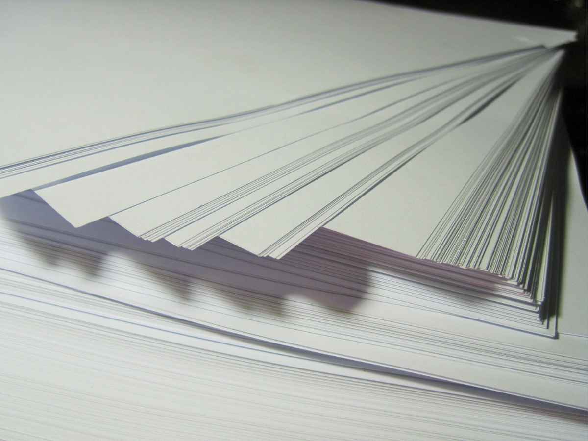 Montagem de uma grande pilha de folhas de papel branco organizadas e parcialmente abertas, representando o coletivo de papéis, resma.