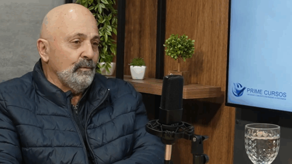 Roberto Manzini participa de um podcast da Prime Cursos, sentado diante de um microfone em estúdio com plantas ao fundo.