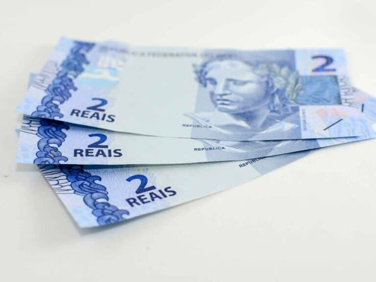 Três cédulas de dois reais sobre superfície branca, representando dinheiro em espécie