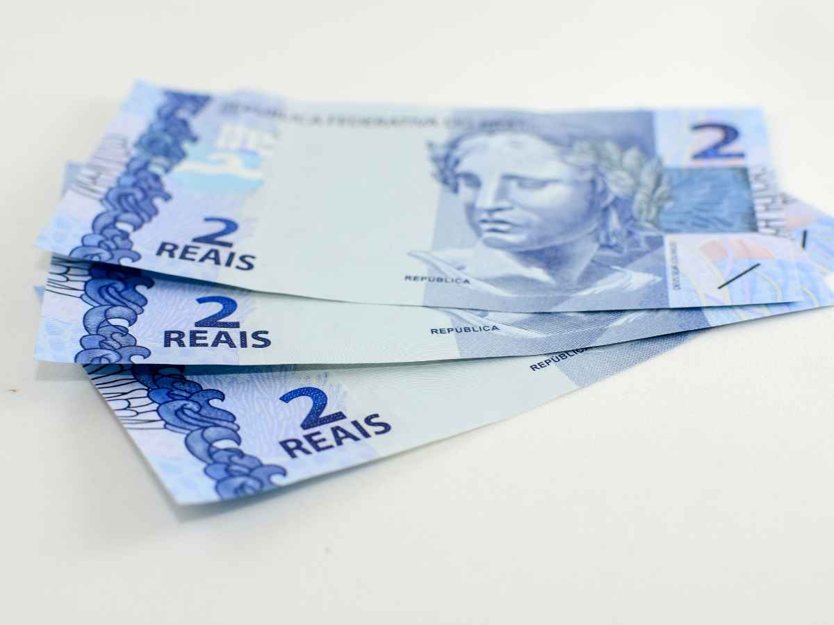 Três cédulas de dois reais sobre superfície branca, representando dinheiro em espécie