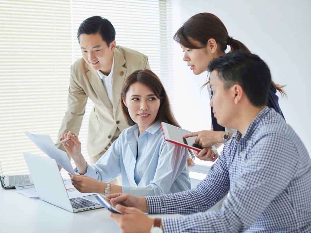 Grupo de profissionais reunidos em uma sala de reunião, discutindo documentos e utilizando notebook e tablet