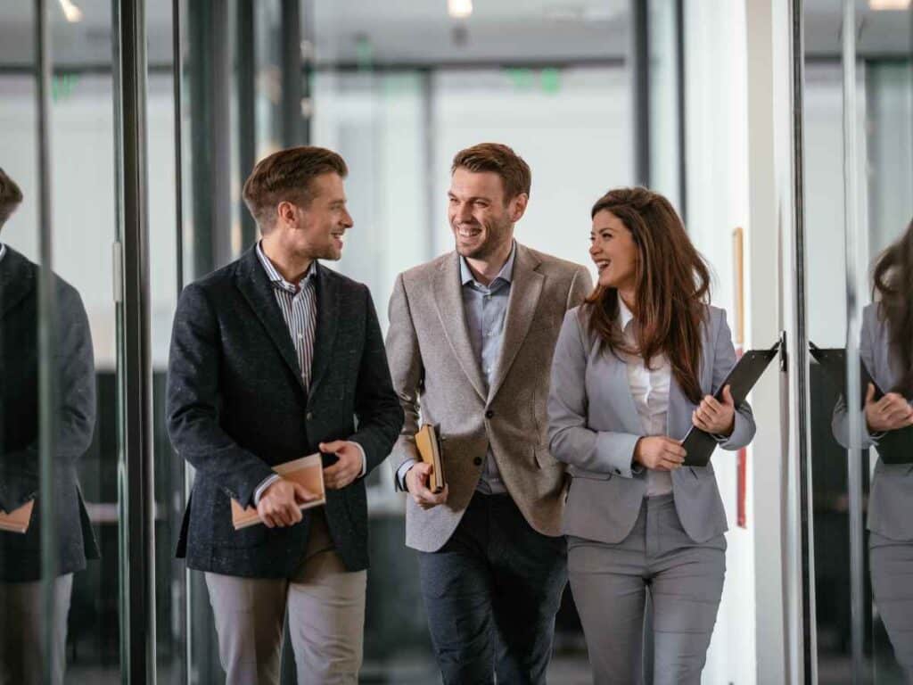 Três profissionais caminhando juntos e conversando com expressões de entusiasmo