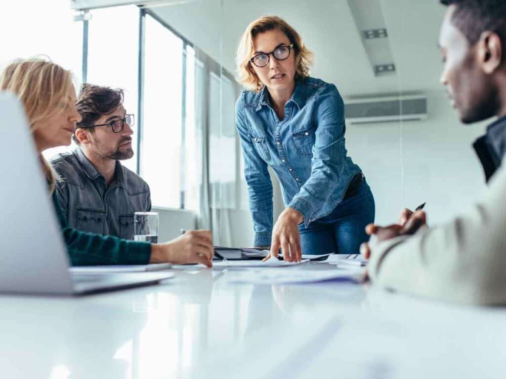 Líder apontando documentos sobre a mesa enquanto orienta sua equipe durante uma reunião