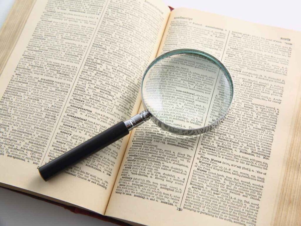 Lupa posicionada sobre um dicionário aberto, ampliando parte do texto impresso nas páginas