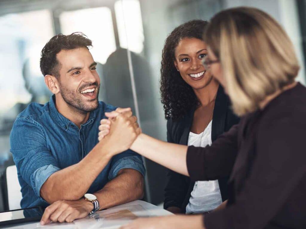 Profissionais sorrindo e apertando as mãos em ambiente corporativo, representando bom relacionamento interpessoal