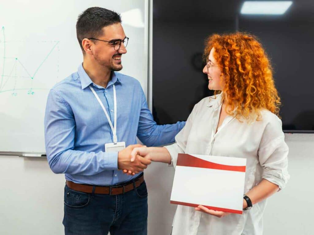 Homem e mulher apertam as mãos enquanto ela segura um certificado