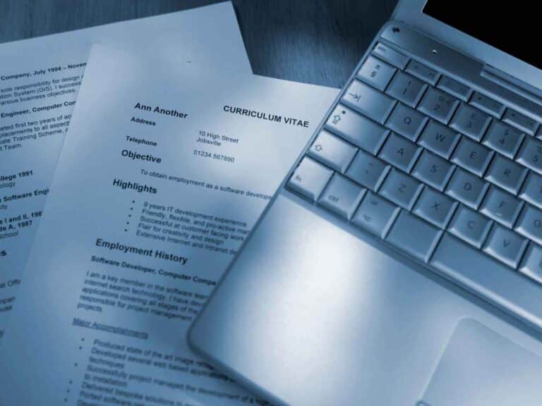 Currículo impresso ao lado de um notebook, representando preparação para candidatura a vaga de emprego.