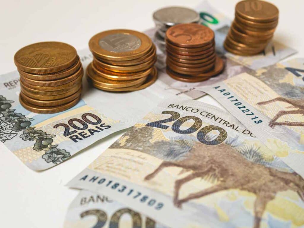 Pilhas de moedas sobre cédulas de 200 reais, representando economia e organização financeira.