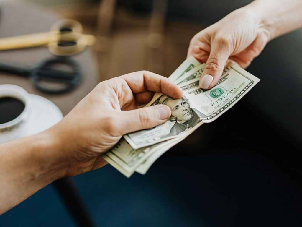 Mãos trocando notas de dólar, simbolizando pagamento em dinheiro ou transação financeira.