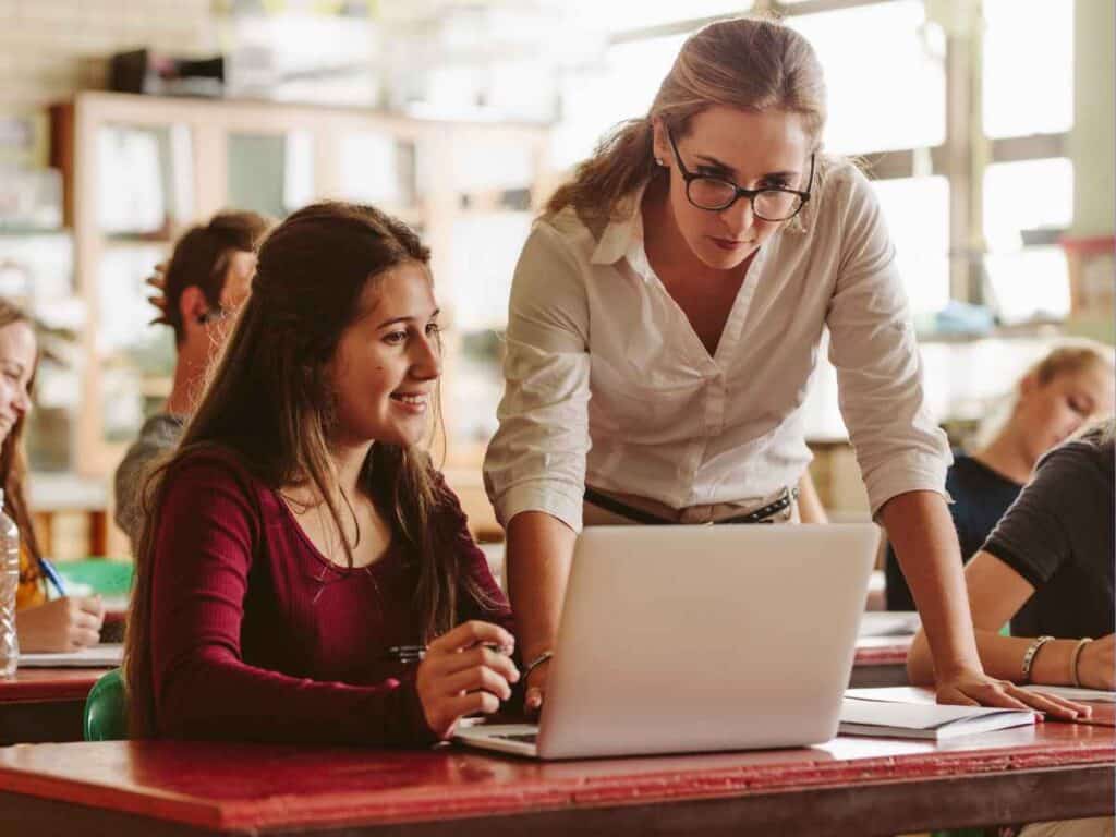 Professora orienta aluna em sala de aula utilizando notebook
