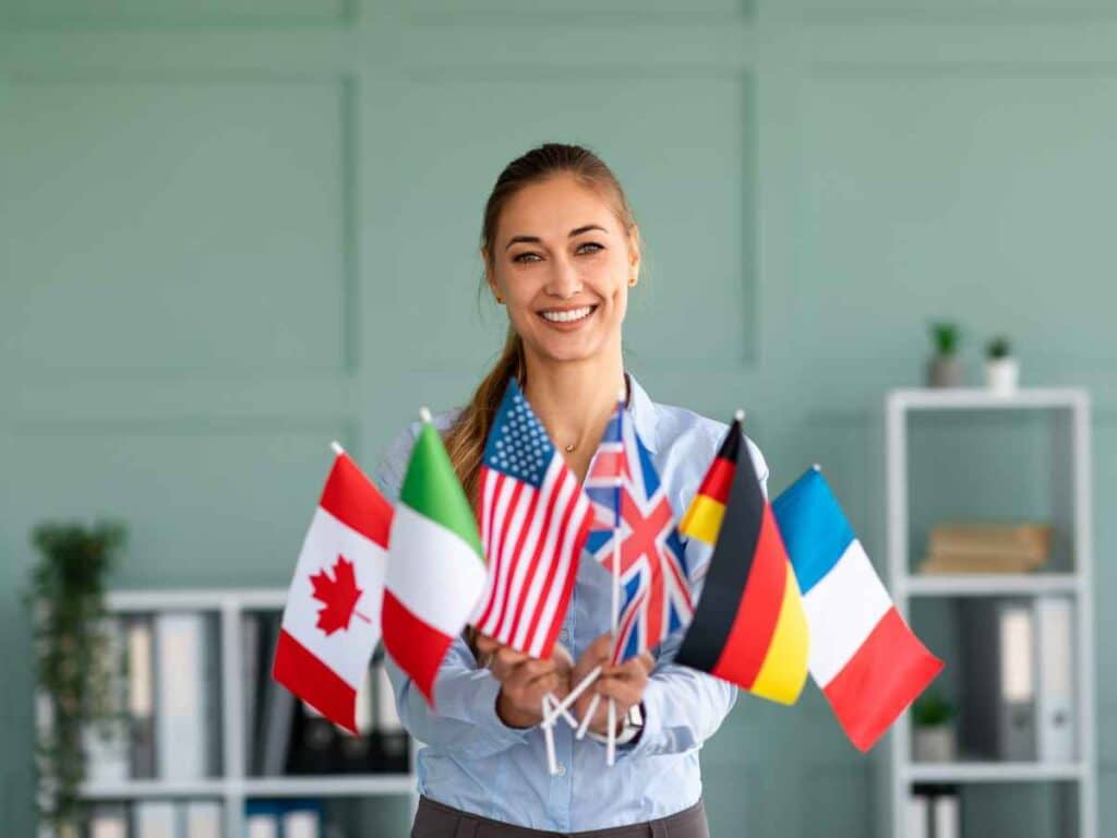 Mulher sorridente segurando pequenas bandeiras de diferentes países, representando ensino de idiomas