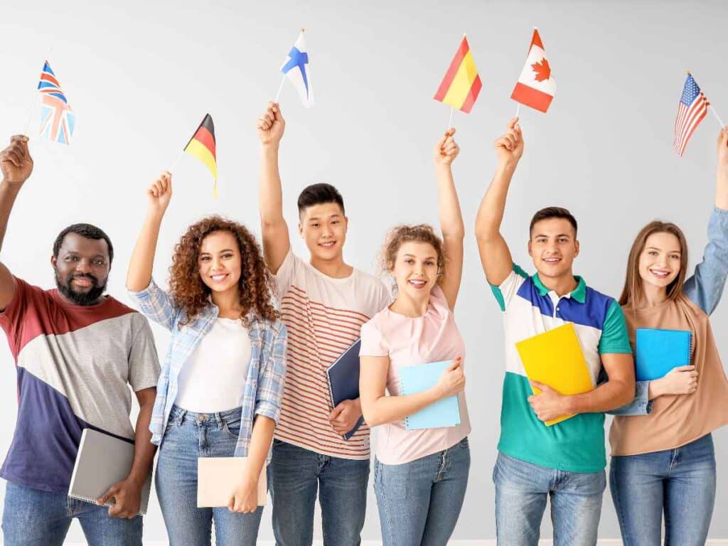 Grupo de estudantes diversos segurando bandeiras internacionais e cadernos, simbolizando aprendizado de idiomas.