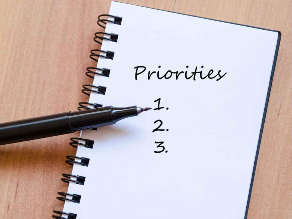 Caderno aberto com a palavra “priorities” e uma lista numerada, acompanhado de caneta, simbolizando definição de prioridades e planejamento de atividades.