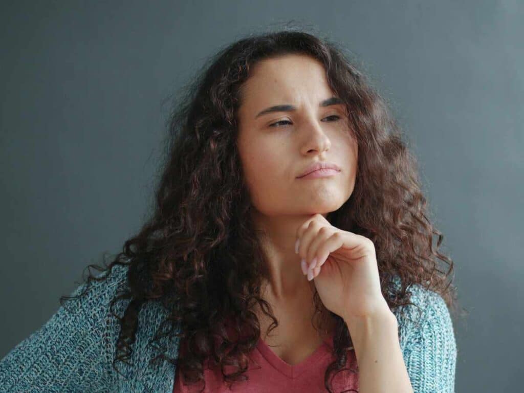 Mulher com expressão pensativa apoiando a mão no queixo, representando dúvida