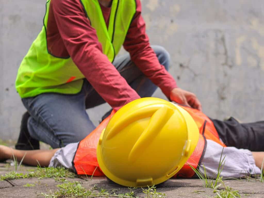 Trabalhador presta os primeiros socorros a um colega caído no chão após um acidente de trabalho